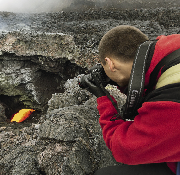 A tourist takes pictures of a well in the top of the lava tube of Flat Tolbachik Volcano.